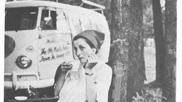 Photo of Margarete sipping tea during a roadside stop. Bill's Volkswagen bus is parked behind in a wooded area.